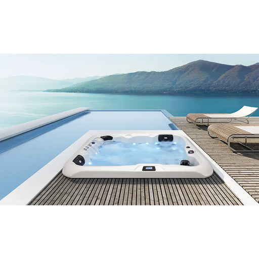 Portcril Double 520 Spa Premium Whirlpool mit weißem Rahmen und schwarzen Düsen am Holzdeck mit Seeblick