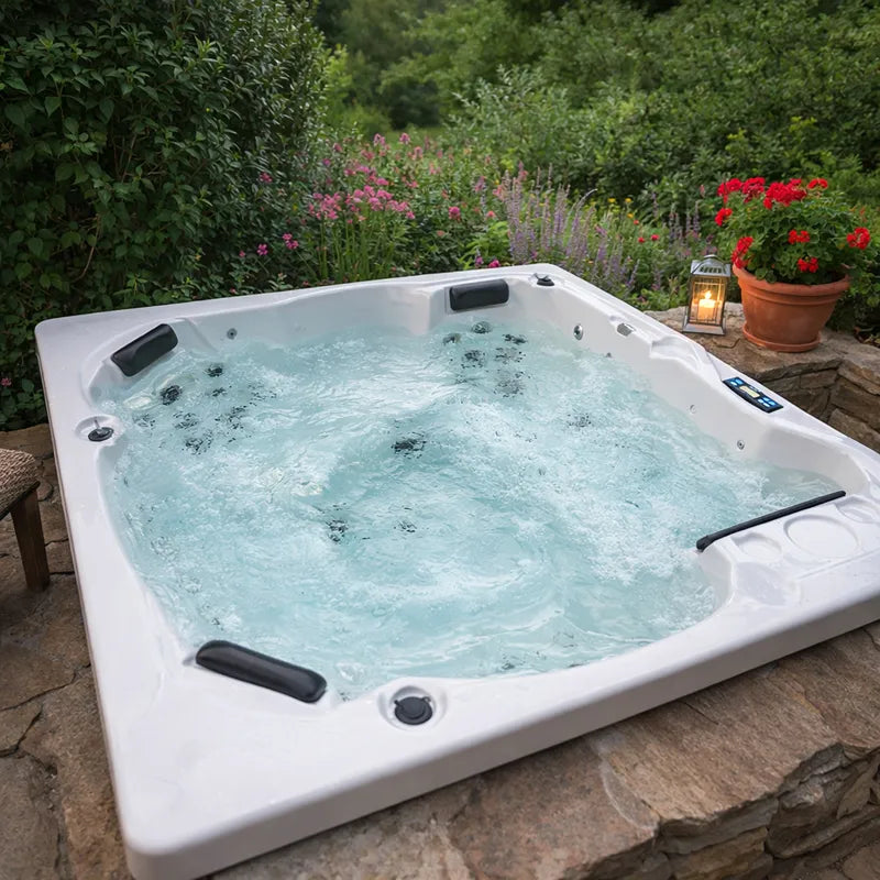 Portcril Emotion 5 Whirlpool für 5 Personen mit sprudelndem Wasser, eingebaut in eine Naturstein-Terrasse, umgeben von blühendem Garten mit Kerzenlaterne.