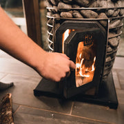 HUUM Hive Wood Holzsaunaofen mit brennendem Feuer, Saunasteine sichtbar, Außenbefeuerung