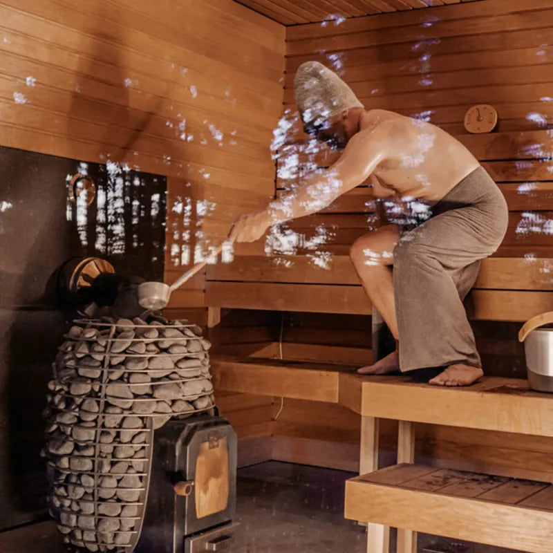 HUUM Hive Wood Holzsaunaofen in Innensauna mit Dampf und Person auf Holzbank
