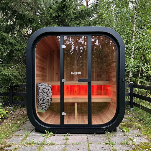 Swedish Cold Grand Escape Gartensauna 4 Personen 90°C mit schwarzem Außenrahmen, Holzinnenraum und roter Infrarotheizung im Garten