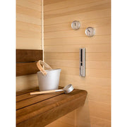 Tylö Brilliant Sauna-Set Eimer & Kelle Silber in Saunakabine, weißer Eimer mit Holzgriff und silberne Kelle auf Holzbank