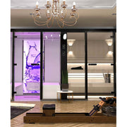 Showroom-Szenerie mit Tylö Dampfbad Panacea Twin, links mit violetter LED-Beleuchtung und Wasserspiel-Design, rechts helle Sauna mit Holzausstattung, elegante Deckenleuchte, Rudergerät im Vordergrund