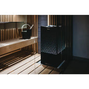 Tylö Crown Combi Saunaofen mit schwarzem Perforationsdesign in moderner Sauna mit Holzbank und Aufgusseimer