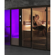 Tylö Panacea Twin Sauna und Dampfbad mit schwarzem Rahmen, links violett leuchtende Dampfkabine, rechts Holzsauna mit zwei Personen, modernes Wellness-System in grauem Badezimmer