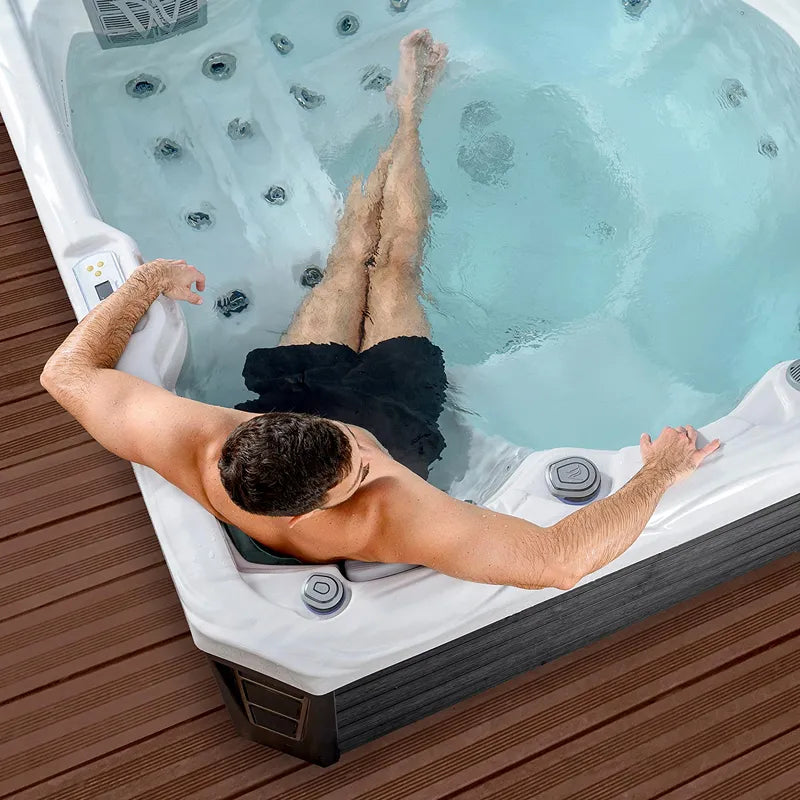 Man relaxing in Wellis Budapest Life Hot Tub with bubbling massage jets and turquoise-blue water on wooden deck
