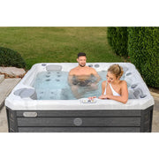 Wellis Budapest Life Whirlpool mit zwei Personen im Garten, weiße Wanne mit grauen Seitenpaneelen und Düsen
