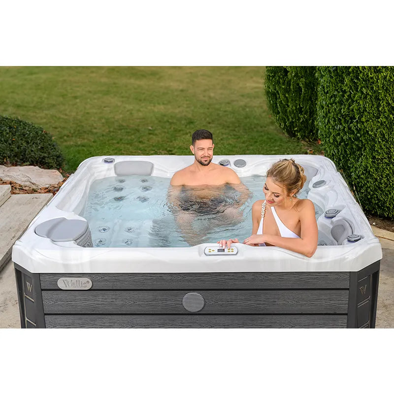 Wellis Budapest Life Whirlpool mit zwei Personen im Garten, weiße Wanne mit grauen Seitenpaneelen und Düsen