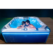 Wellis Elbrus Life Premium Whirlpool mit 7 Sitzen und 61 Jets, zwei Personen entspannen im beleuchteten Whirlpool im Garten