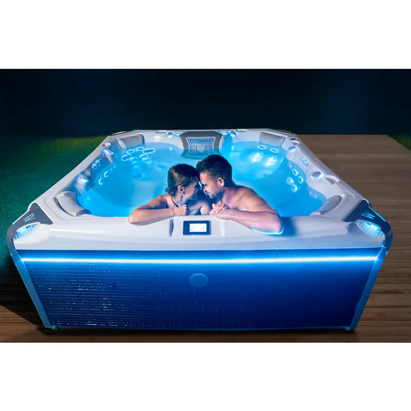 Wellis Elbrus Life Premium Whirlpool mit 7 Sitzen und 61 Jets, zwei Personen entspannen im beleuchteten Whirlpool im Garten