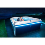 Wellis Elbrus Life Premium Whirlpool mit 7 Sitzen und 61 Jets, zwei Personen entspannen nachts im beleuchteten Whirlpool auf Holzterrasse