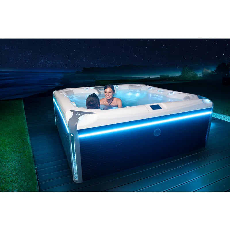 Wellis Elbrus Life Premium Whirlpool mit 7 Sitzen und 61 Jets, zwei Personen entspannen nachts im beleuchteten Whirlpool auf Holzterrasse