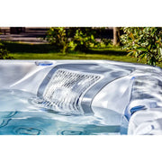 Wellis Everest Life Premium Whirlpool mit weißem Rand und blauen Akzenten, befüllt mit türkisblauem Wasser, im sonnigen Garten
