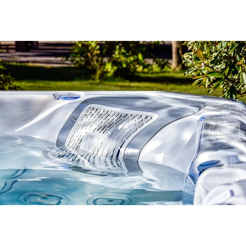 Wellis Everest Life Premium Whirlpool mit weißem Rand und blauen Akzenten, befüllt mit türkisblauem Wasser, im sonnigen Garten