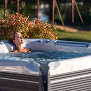 Frau entspannt im Wellis Everest Life Premium Whirlpool mit 68 Jets im sonnigen Garten, umgeben von Blüten und Grün
