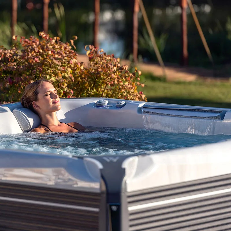 Frau entspannt im Wellis Everest Life Premium Whirlpool mit 68 Jets im sonnigen Garten, umgeben von Blüten und Grün