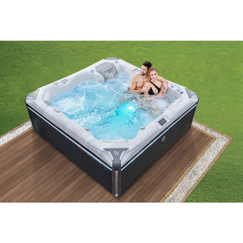 Wellis Kilimanjaro Life Premium Whirlpool mit 6 Sitzen und 59 Jets im Garten auf Holzterrasse, zwei Personen genießen sprudelndes Wasser