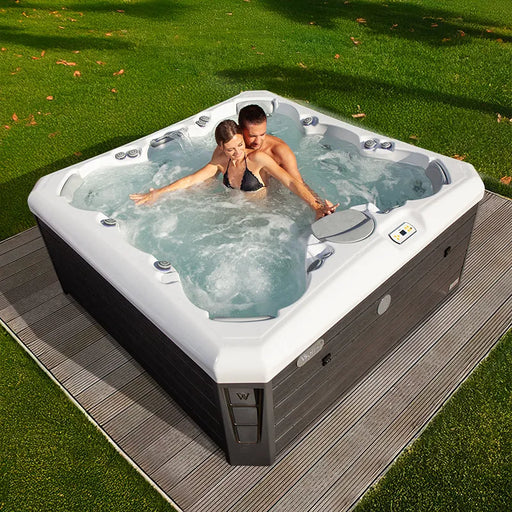 Wellis Lima Life Premium-Whirlpool mit zwei Personen im sprudelnden Wasser, weiß-schwarzes Design auf Holzdeck im Garten