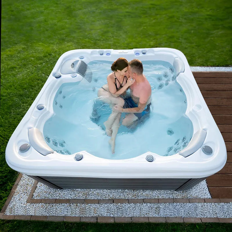 Wellis Lugano Life Premium-Whirlpool mit zwei Personen im Garten, sprudelnde Düsen und blaues Wasser sichtbar