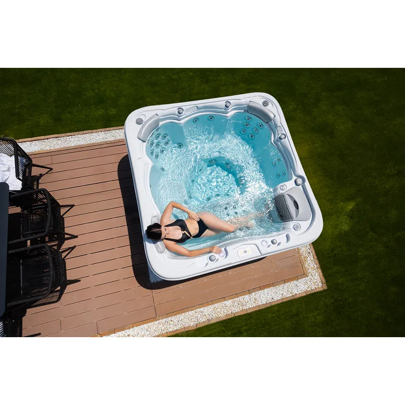 Wellis Lugano Life Premium-Whirlpool mit sprudelndem Wasser auf Holzterrasse neben Rasen, eine Person genießt das warme Wasser