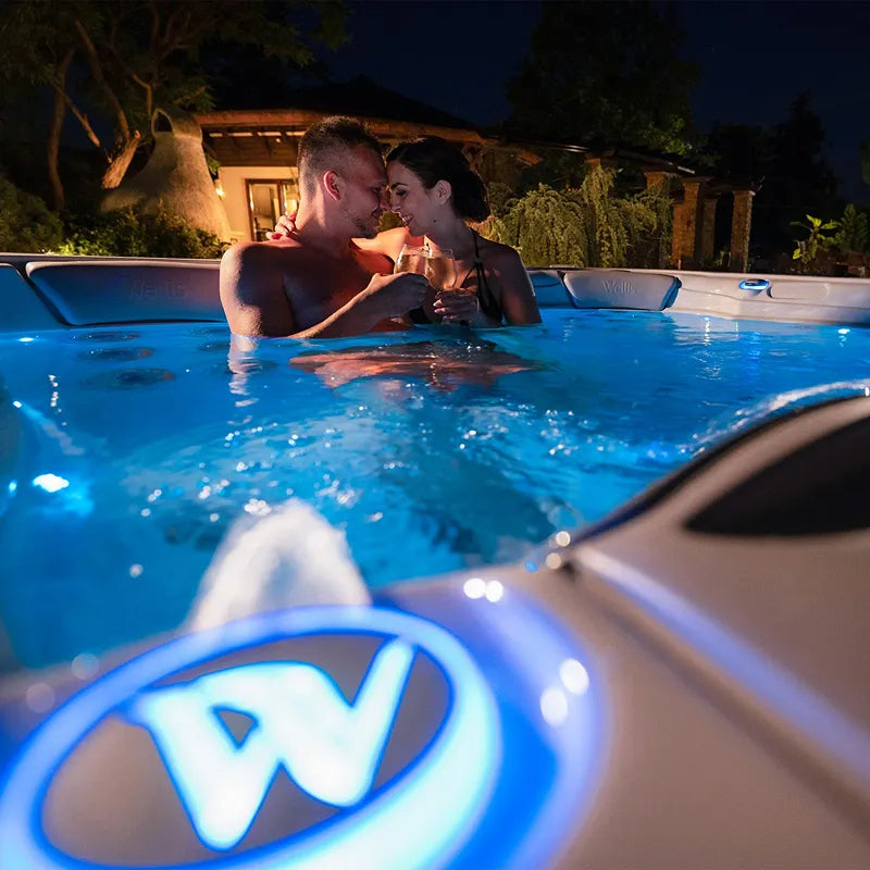 Wellis Lugano Life Premium Hot Tub with couple at night in illuminated garden with garden shed