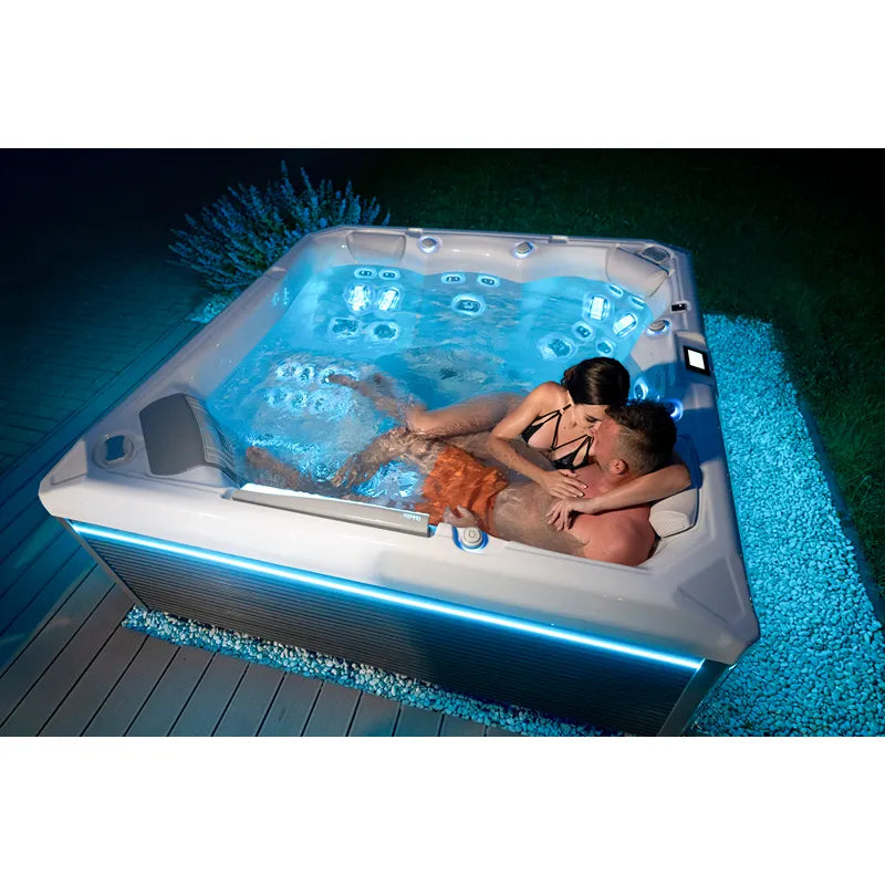 Wellis Makalu Life Premium Whirlpool mit Paar im warmen Wasser, beleuchtet durch LED-Effekte bei Nacht im Garten