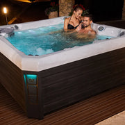 Wellis Palermo Life Premium-Whirlpool mit zwei Personen im türkisblauen Wasser auf Terrasse bei Nacht
