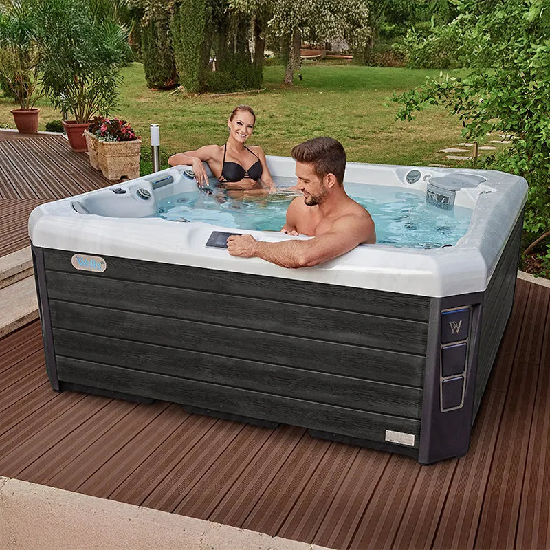 Wellis Palermo Life Premium-Whirlpool mit zwei Personen in Gartensetting auf Holzterrasse
