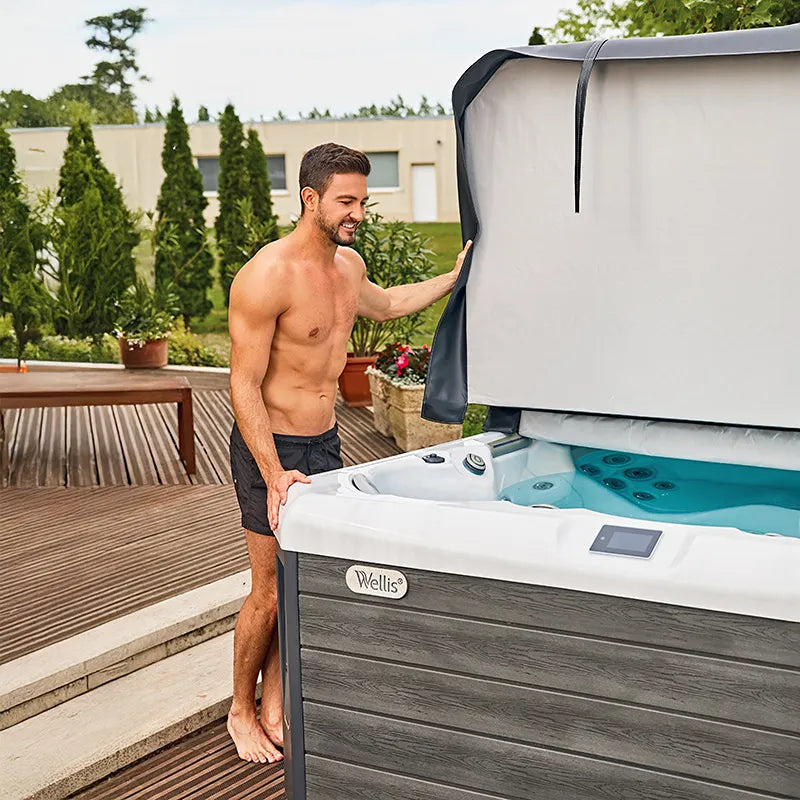 Mann nutzt Wellis Palermo Life Premium-Whirlpool mit türkisblauem Wasser auf Holzterrasse im Garten