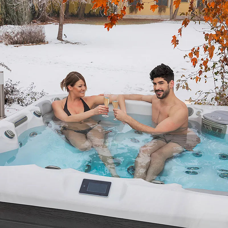 Wellis Palermo Life Premium-Whirlpool mit zwei Personen im winterlichen Garten, Schnee im Hintergrund und herbstliche Vegetation
