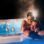Wellis Teide Life Whirlpool mit Paar beim entspannen im warmen Wasser bei Nacht, beleuchtete Jets und Champagergläser