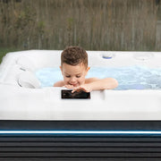 Kind sitzt im Wellis Teide Life Premium Whirlpool und bedient das Kontrollpanel, umgeben von Wald