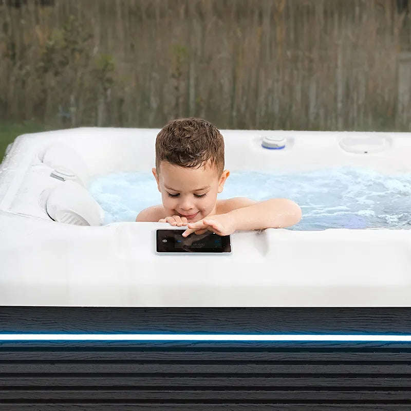 Kind sitzt im Wellis Teide Life Premium Whirlpool und bedient das Kontrollpanel, umgeben von Wald