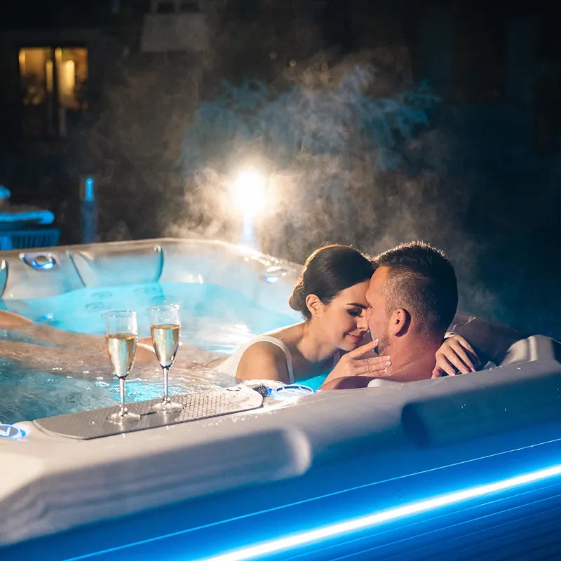 Wellis Teide Life Whirlpool mit Paar bei Nacht, dampfend, Champagergläser am Rand