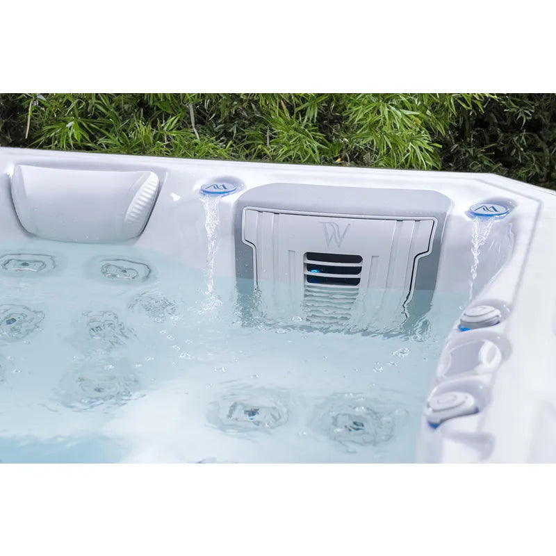 Wellis Teide Life Premium Whirlpool mit 32 Jets und aktiven Wasserfontänen im Garten, umgeben von grünen Hecken