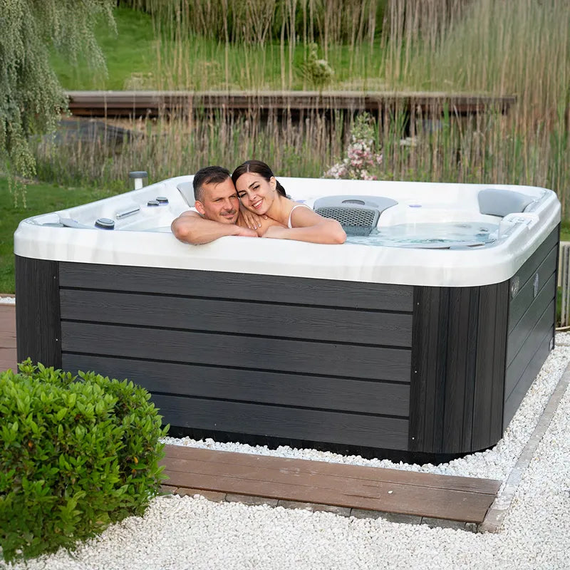 Wellis Vienna Life Premium-Whirlpool mit Paar im Garten, schwarze Holzverkleidung, weiße Innenausstattung