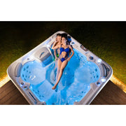 Wellis Vienna Life Premium-Whirlpool mit zwei Personen in beleuchtetem Wasser auf Holzterrasse im Garten
