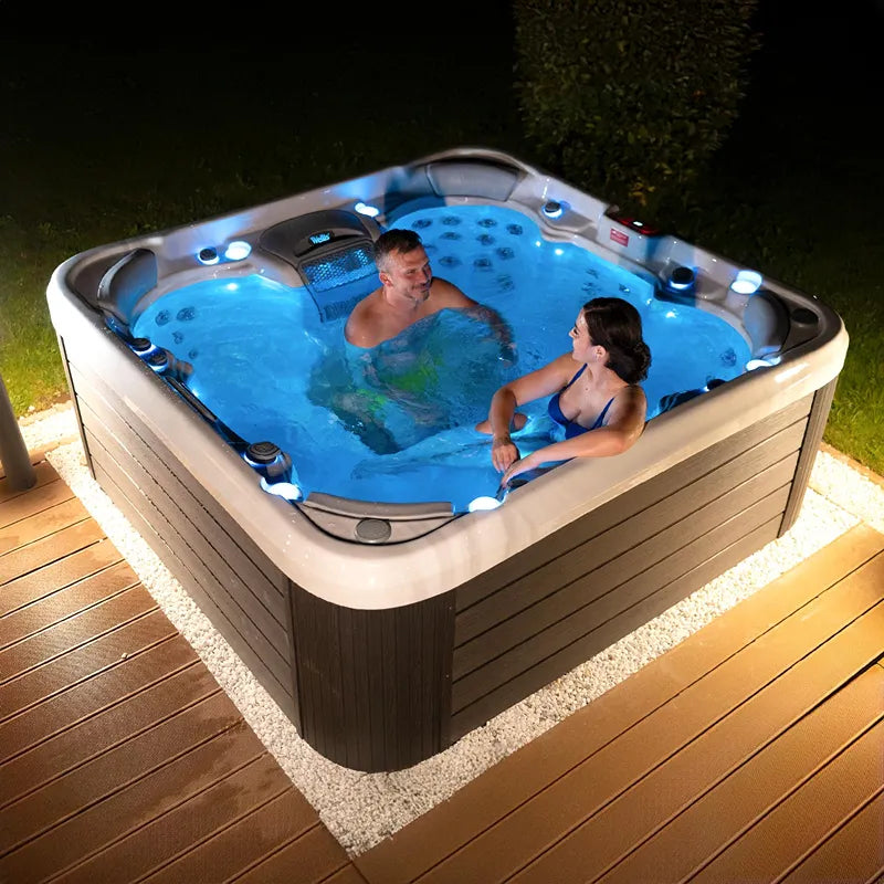 Wellis Vienna Life Premium-Whirlpool mit zwei Personen in blauem Wasser auf beleuchteter Terrasse