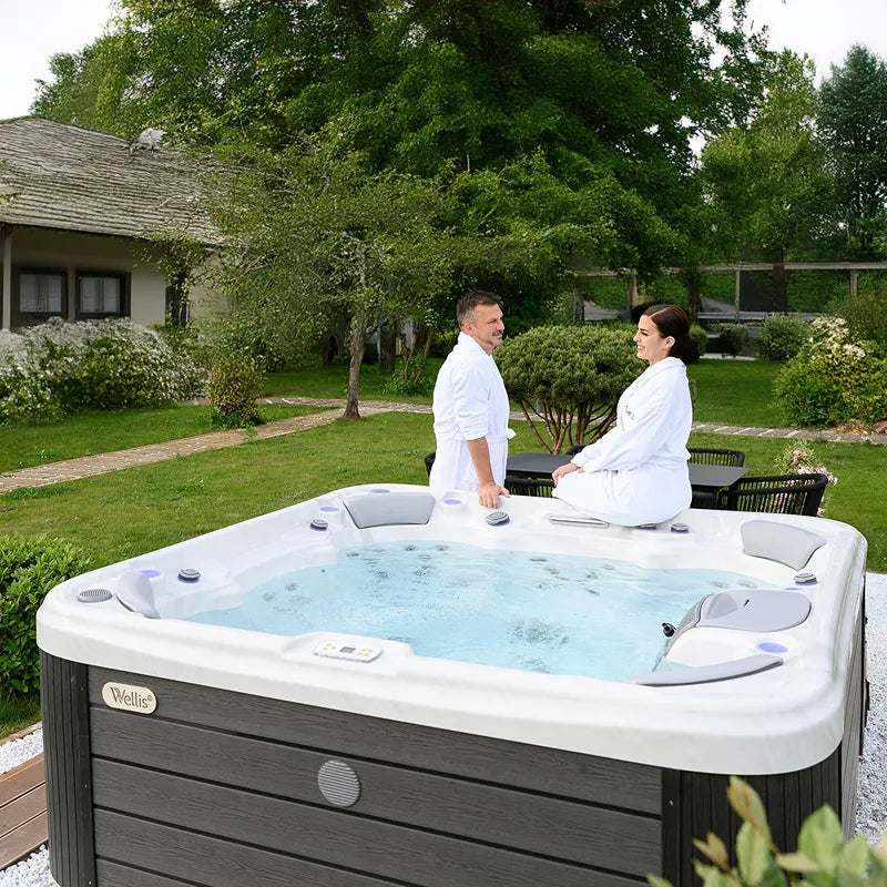Wellis Vienna Life Premium-Whirlpool mit zwei Personen im Garten, umgeben von grünen Bäumen und Terrasse