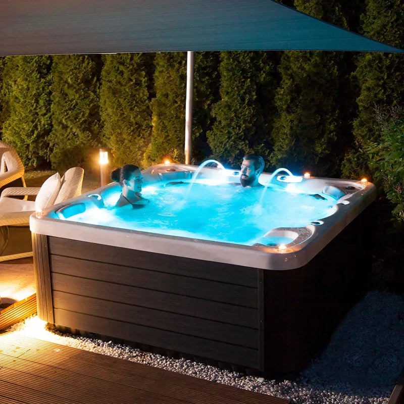 Wellis Jupiter – Classic Line Whirlpool 6 Personen mit LED-Beleuchtung im Garten bei Nacht, zwei Personen entspannen im Whirlpool