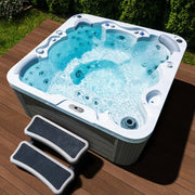 Wellis Jupiter – Classic Line Whirlpool 6 Personen mit sprudelndem Wasser auf Holzterrasse, umgeben von grünen Hecken