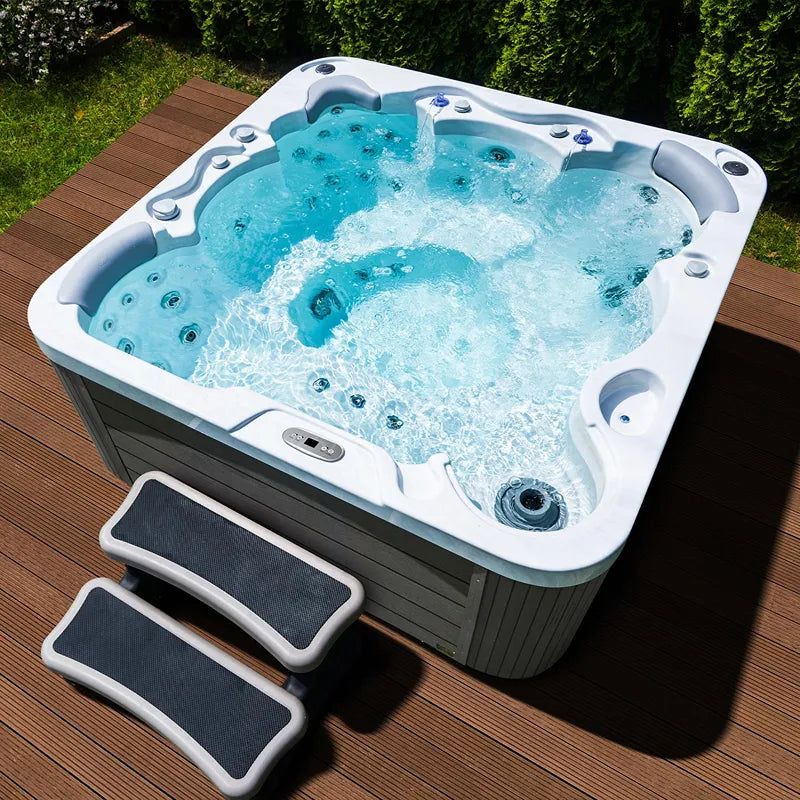Wellis Jupiter – Classic Line Whirlpool 6 Personen mit sprudelndem Wasser auf Holzterrasse, umgeben von grünen Hecken