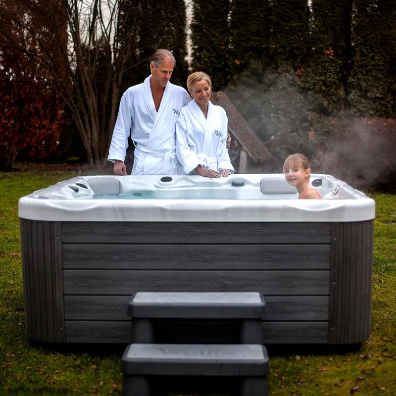 Wellis Pluto – Classic Line Whirlpool 5 Personen mit Familie im Garten, dampfend, Holzverkleidung