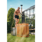 Winthera Arctic Barrel Eisbad Holzfass: Mann steigt in das Wellness-Holzfass mit Leiter im Garten ein